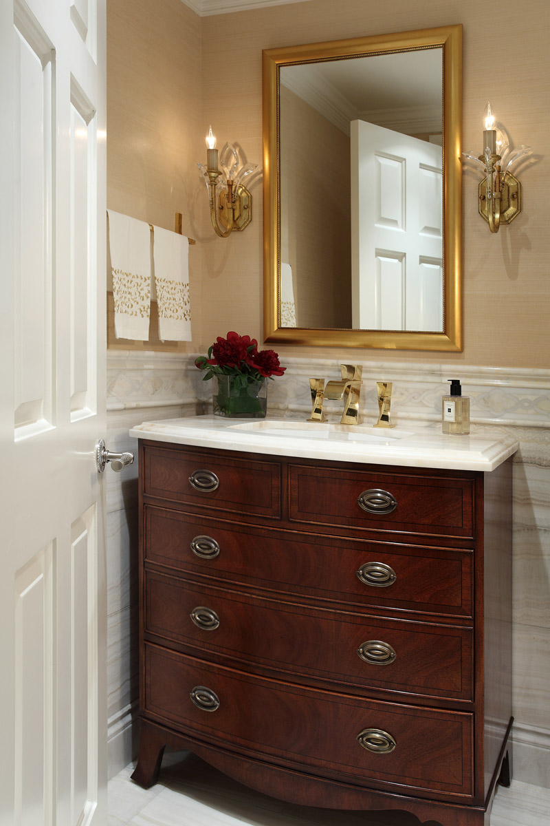 Powder room custom wood cabinetry with gold rectangular mirror and faucet. Two crystal sconces on each side of mirror.